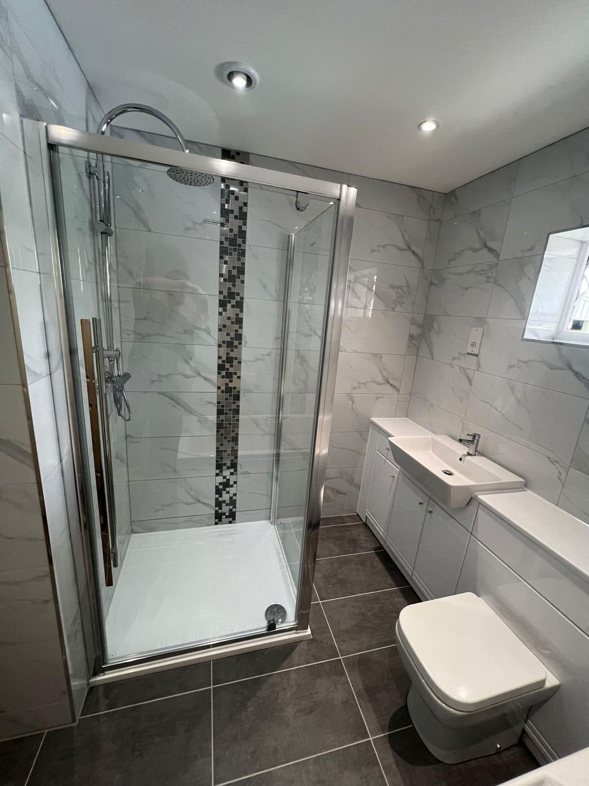 Marble-effect shower room with a glass enclosure and mosaic band